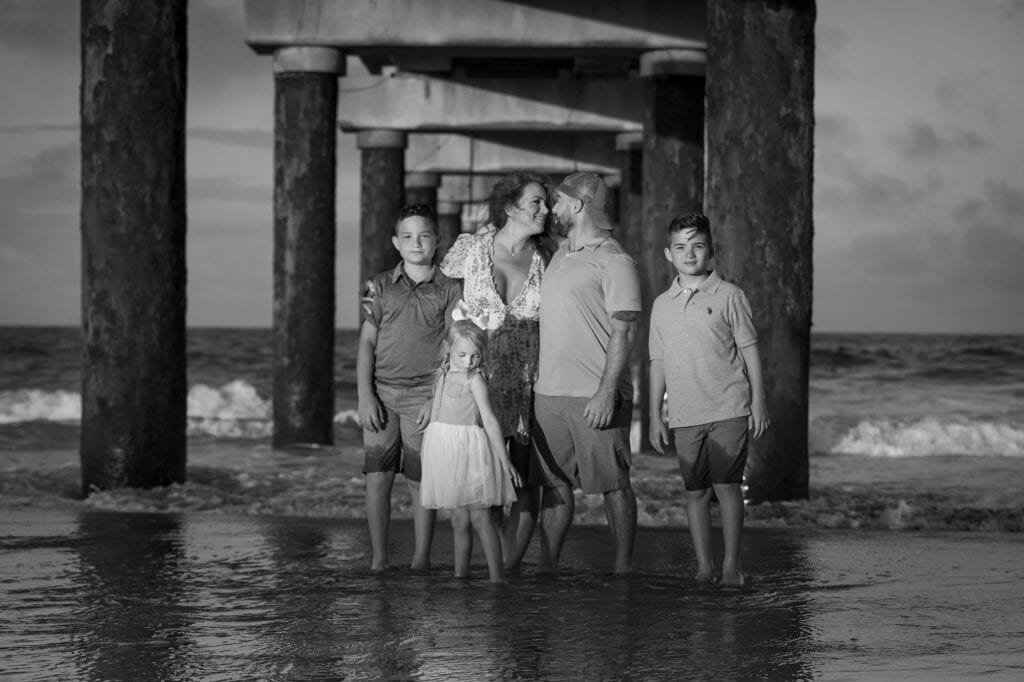 Family under a pier on the beach at sunset