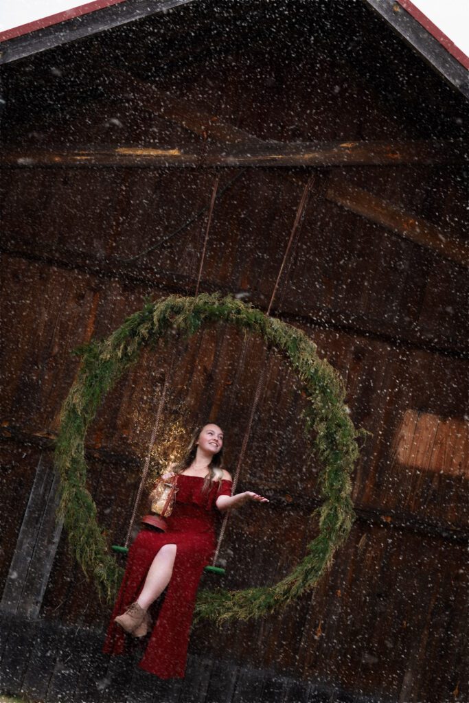 Girl on wreath swing hanging on old barn in the snow