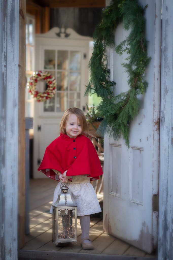 Little girl in the doorway of a small country home with a Christmas wreath