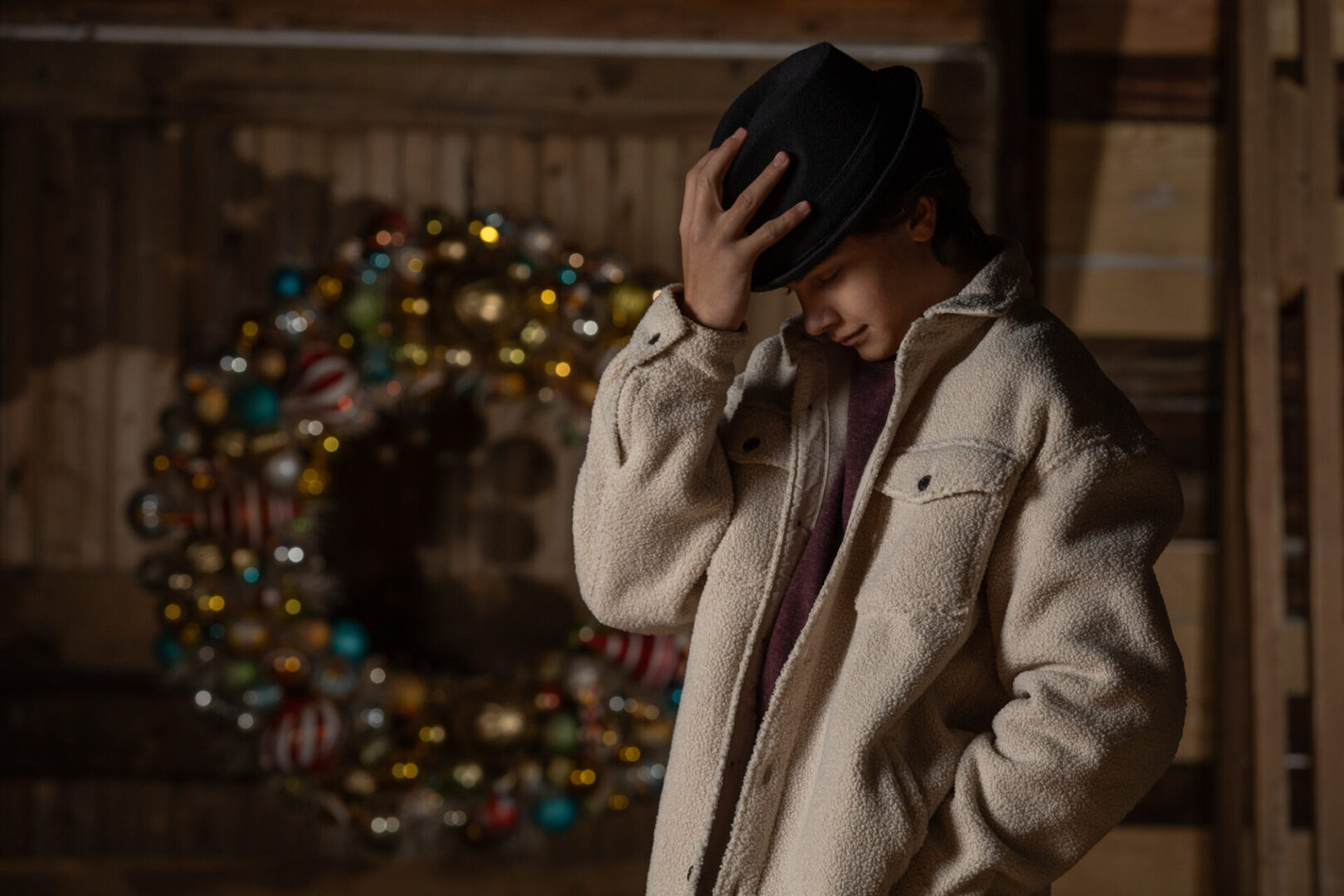 Young man in festive hat with large Christmas wreath, in an old barn