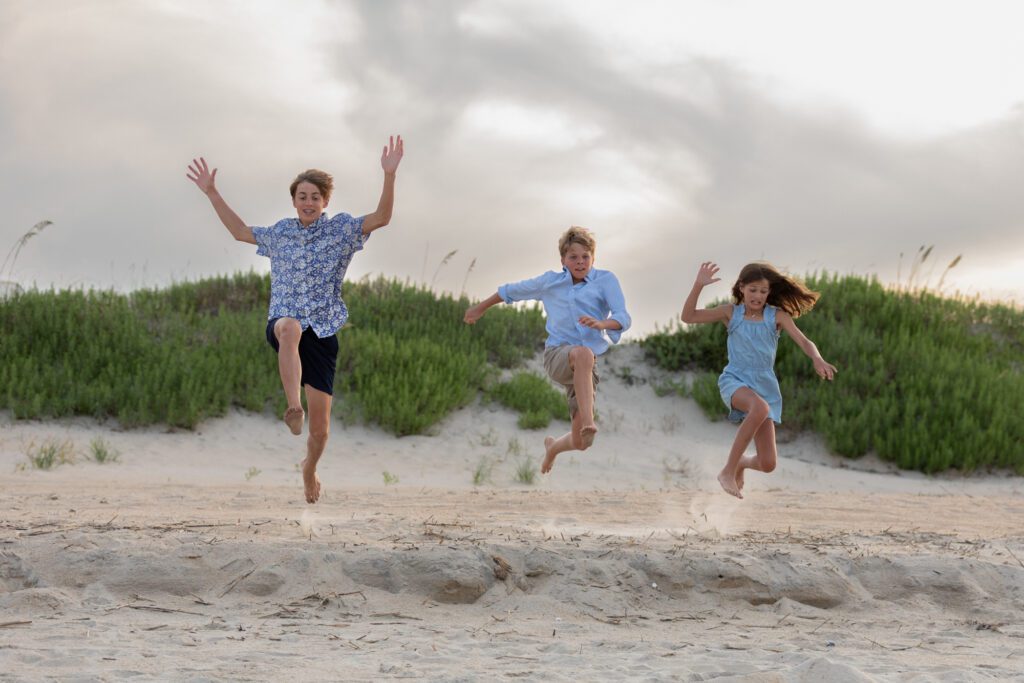 girl jumping on the beach with her older brothers in Duck, Nc