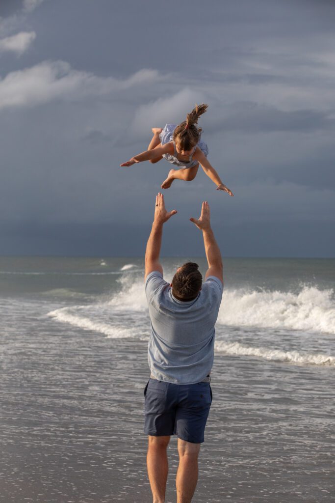 Dad throwing young girls on the beach in Duck, NC in the beautiful evening light