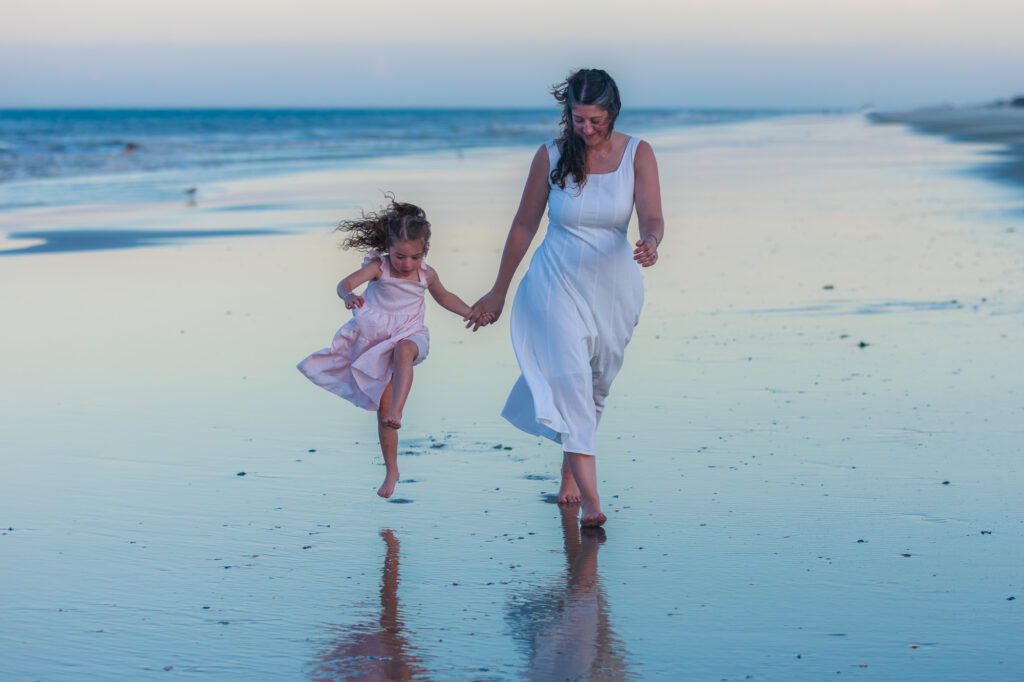 Mother and daughter skipping on the beach at sunset