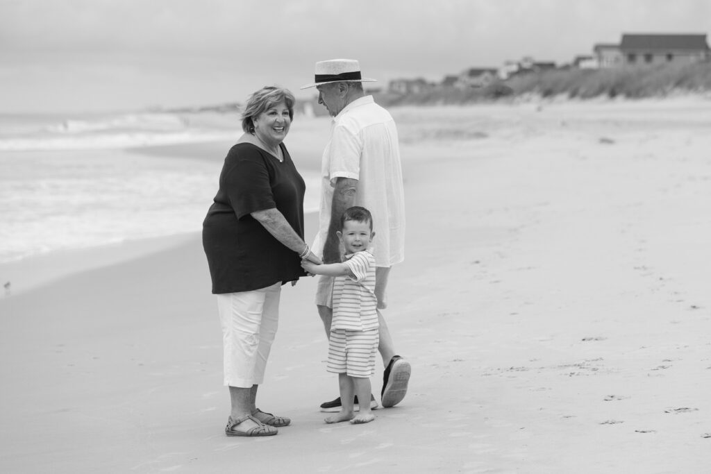 Black and white vintage looking image, of grandparents with grandson walking along the beach in Duck, NC
